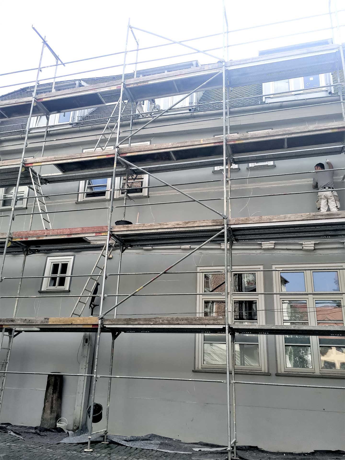 Ein Mann steht auf einem Baugerüst und bearbeitet die Fassade eines Hauses